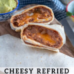 Pinterest Pin with text 'Cheesy Refried Bean Burrito', with image of two halves of a burrito cut open to reveal the inside on a cutting board.