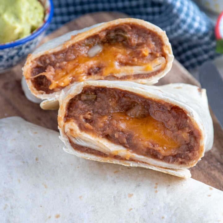 Refried bean burrito cut in half showing the cheesy insides on a cutting board.