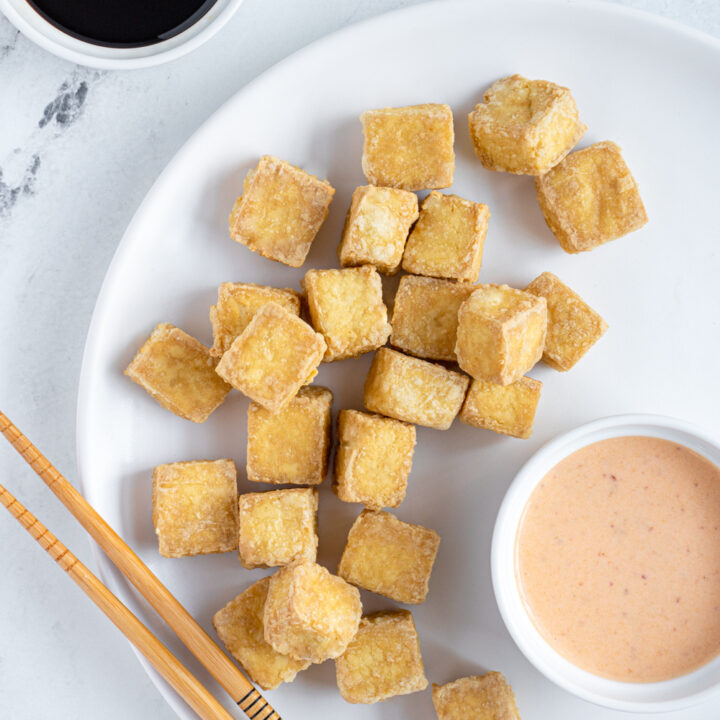 White plate filled with a pile of golden brown crispy tofu from the air fryer.
