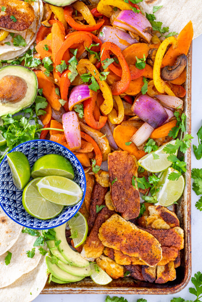 Close up of a tray filled with fajita veggies and golden brown halloumi cheese garnished with lime wedges and cilantro.