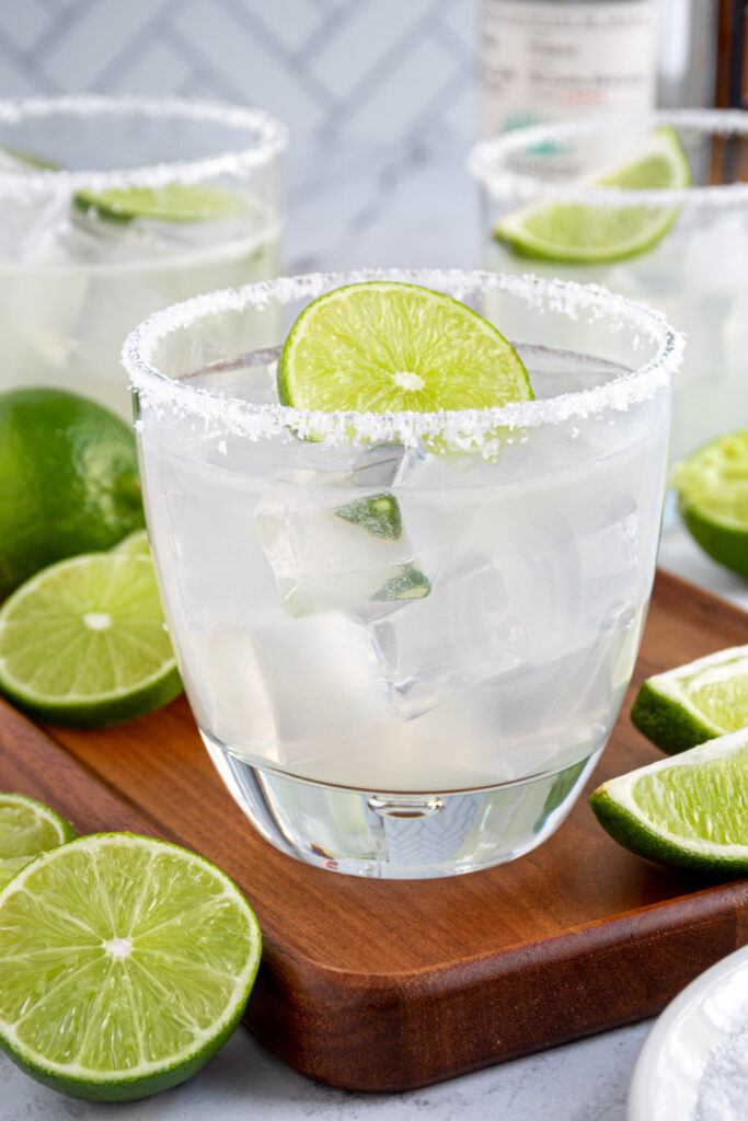 Close up of a glass with a salted rim filled with ice and a margarita cocktail garnished with a lime wheel.