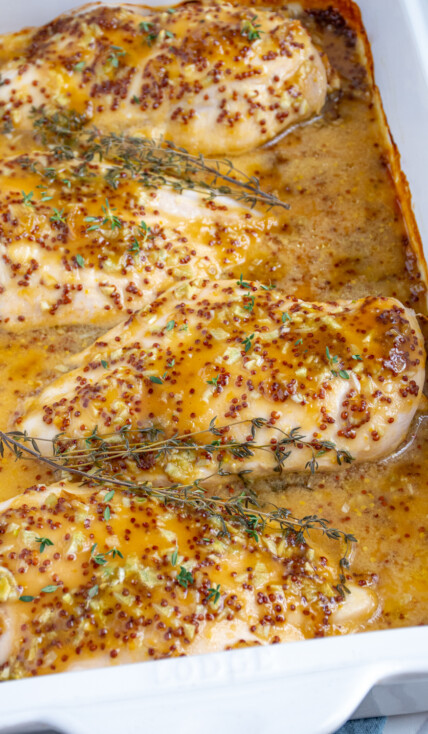 Baked Honey Mustard Chicken in a casserole dish covered in homemade sauce and garnished with fresh thyme.