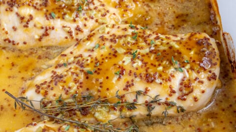 Baked Honey Mustard Chicken in a casserole dish covered in homemade sauce and garnished with fresh thyme.