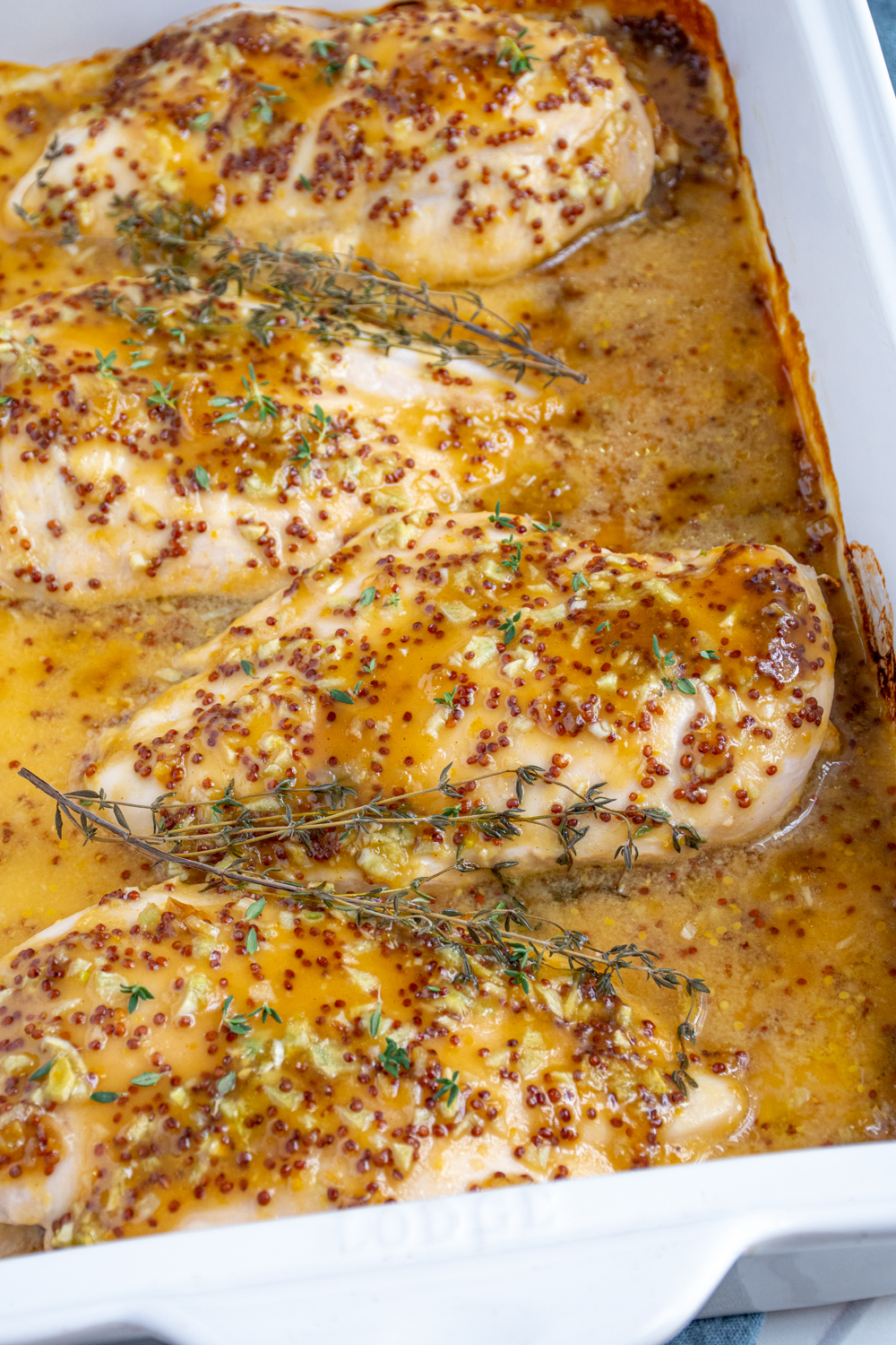 Baked Honey Mustard Chicken in a casserole dish covered in homemade sauce and garnished with fresh thyme.
