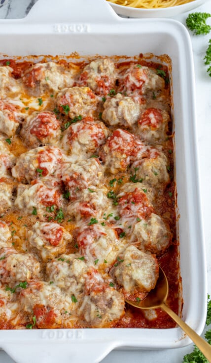 White casserole dish with baked turkey meatballs in sauce covered with cheese and fresh parsley.