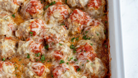 White casserole dish with baked turkey meatballs in sauce covered with cheese and fresh parsley.