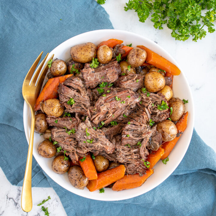 Flatlay showing a large severing bowl filled with slow cooker pot roast with red wine, carrots, and baby potatoes.