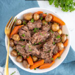 Pinterest Pin with text 'Crockpot Pot Roast', image of a serving bowl with chunks of pot roast, carrots, and baby potatoes.