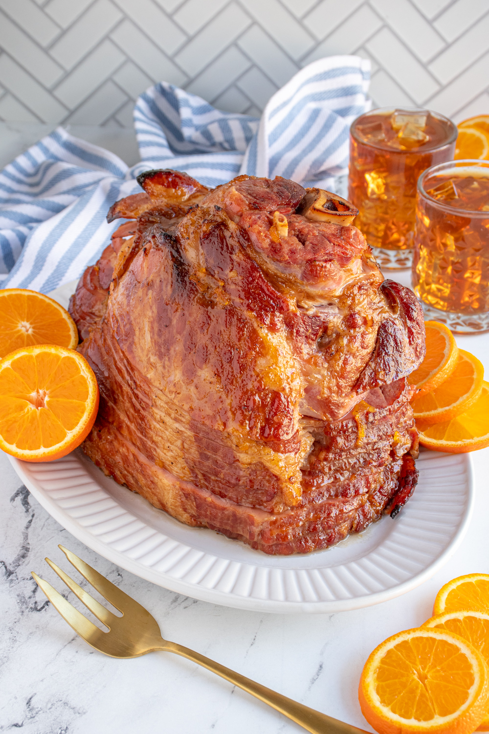 A ham with orange bourbon glaze cooked on, sitting on a white platter and garnished with orange slices.