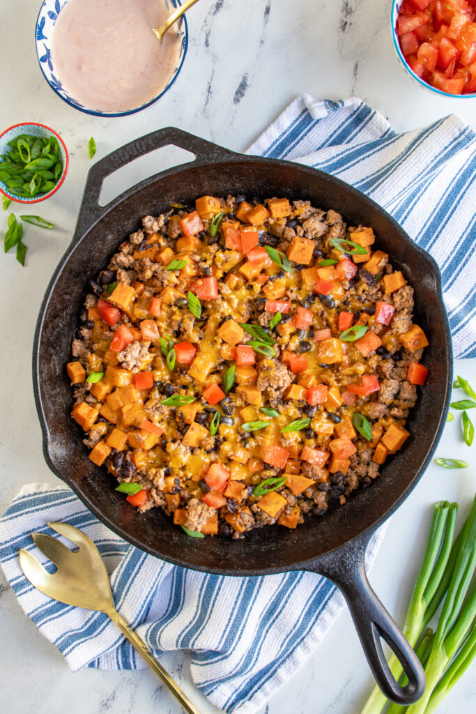 Sweet potatoes and turkey skillet with black beans covered with melted cheddar cheese and topped with diced tomatoes and sliced green onions.