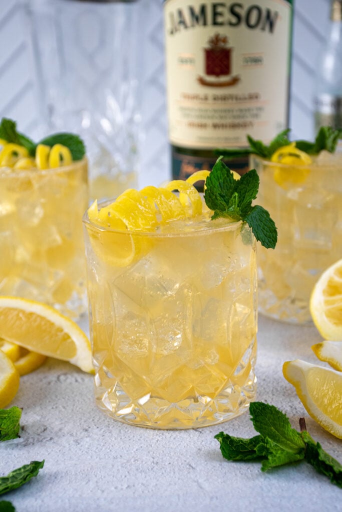 Close up of a whiskey glass full of Irish Lemonade and ice garnished with a lemon peel and mint leaf.