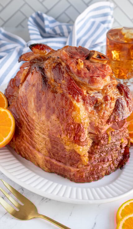 An Orange Bourbon Glazed Ham on a white platter garnished with orange slices.