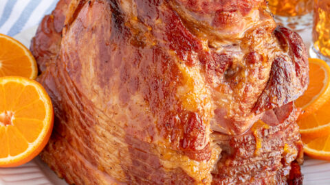 An Orange Bourbon Glazed Ham on a white platter garnished with orange slices.