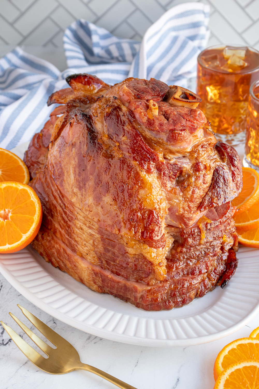 An Orange Bourbon Glazed Ham on a white platter garnished with orange slices.