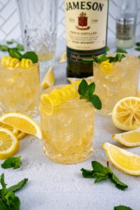Whiskey glasses on a table filled with ice and Irish Lemonades, garnished with lemon peel and mint leaves.