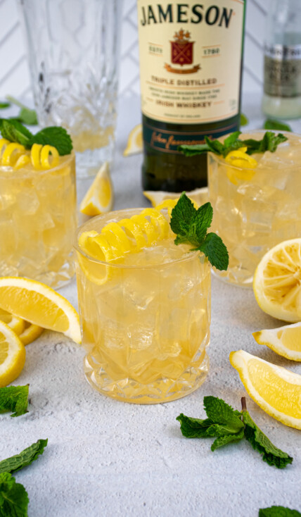 Whiskey glasses on a table filled with ice and Irish Lemonades, garnished with lemon peel and mint leaves.