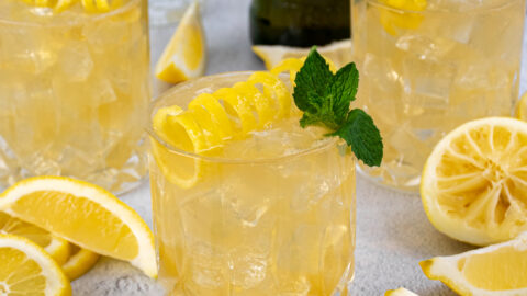 Whiskey glasses on a table filled with ice and Irish Lemonades, garnished with lemon peel and mint leaves.