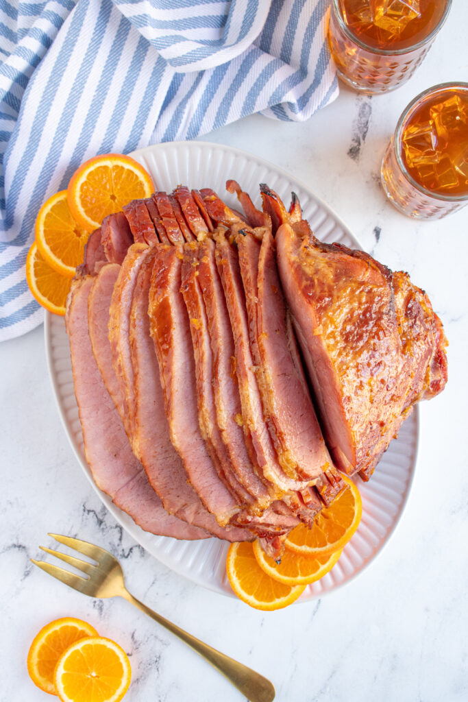Overhead view of an orange bourbon glazed ham on a white platter with the serials open up to see the inside of the ham.