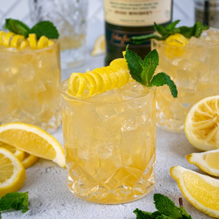 Glasses filled with ice and Irish lemonade cocktail garnished with lemon peel and a mint sprig.