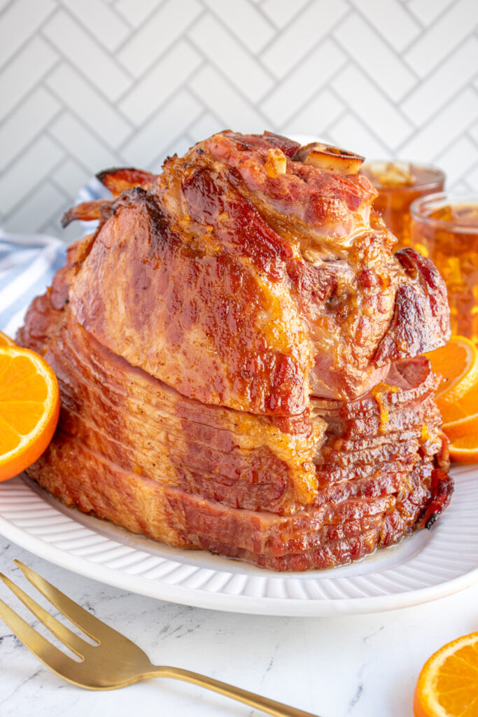 A glazed orange and bourbon ham on a white platter showing off the spiral side shining with glaze.
