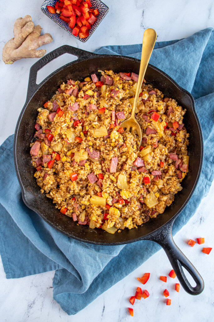 Overhead view of a skillet filled with ham fried rice with pineapples and red bell pepper.