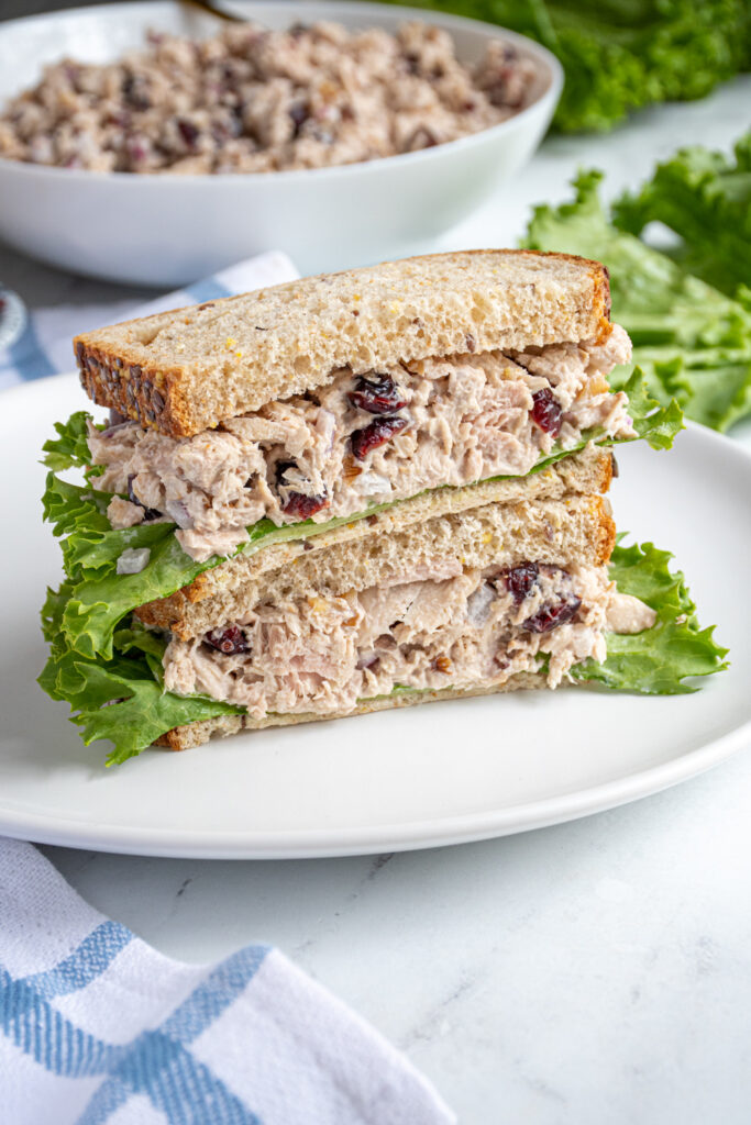A tuna salad sandwich with cranberries cut in half with lettuce, showing the insides of the tuna sandwich.