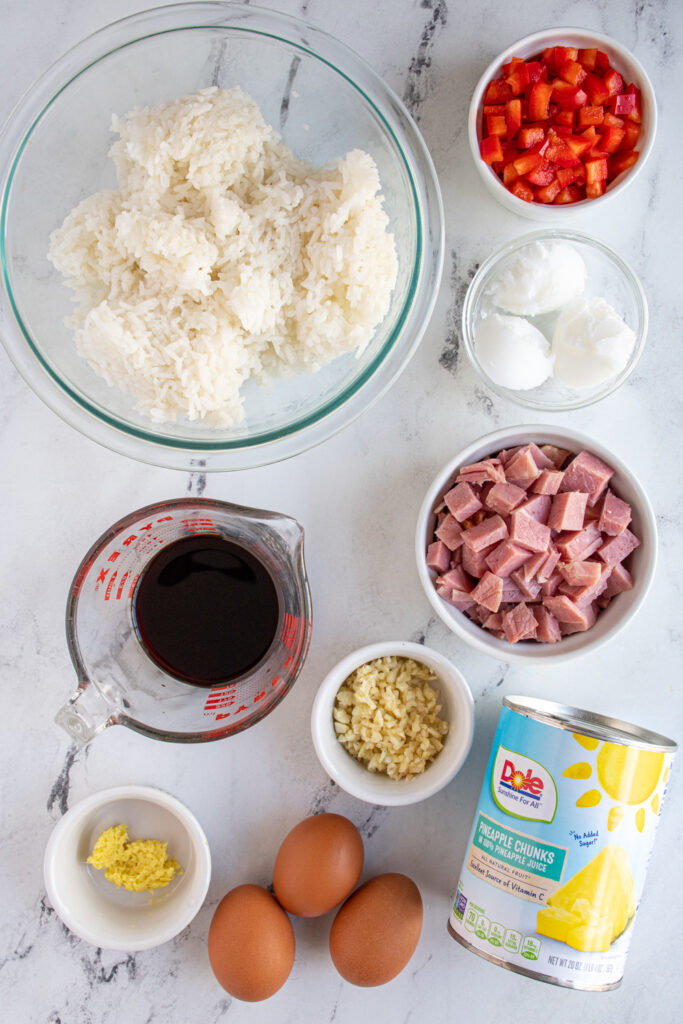 Ingredients for to make ham and pineapple fried rice laid out on a tabletop.