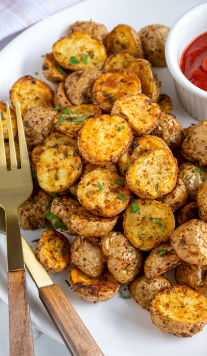 A plate filled with a pile of air fryer home fries with ketchup and a gold fork.