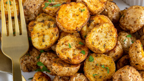 A plate filled with a pile of air fryer home fries with ketchup and a gold fork.