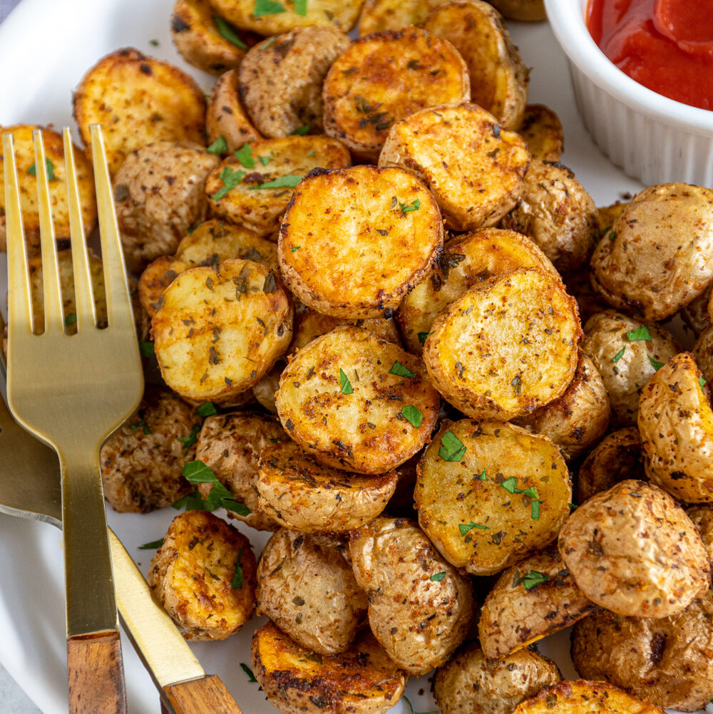 A plate filled with a pile of air fryer home fries with ketchup and a gold fork.