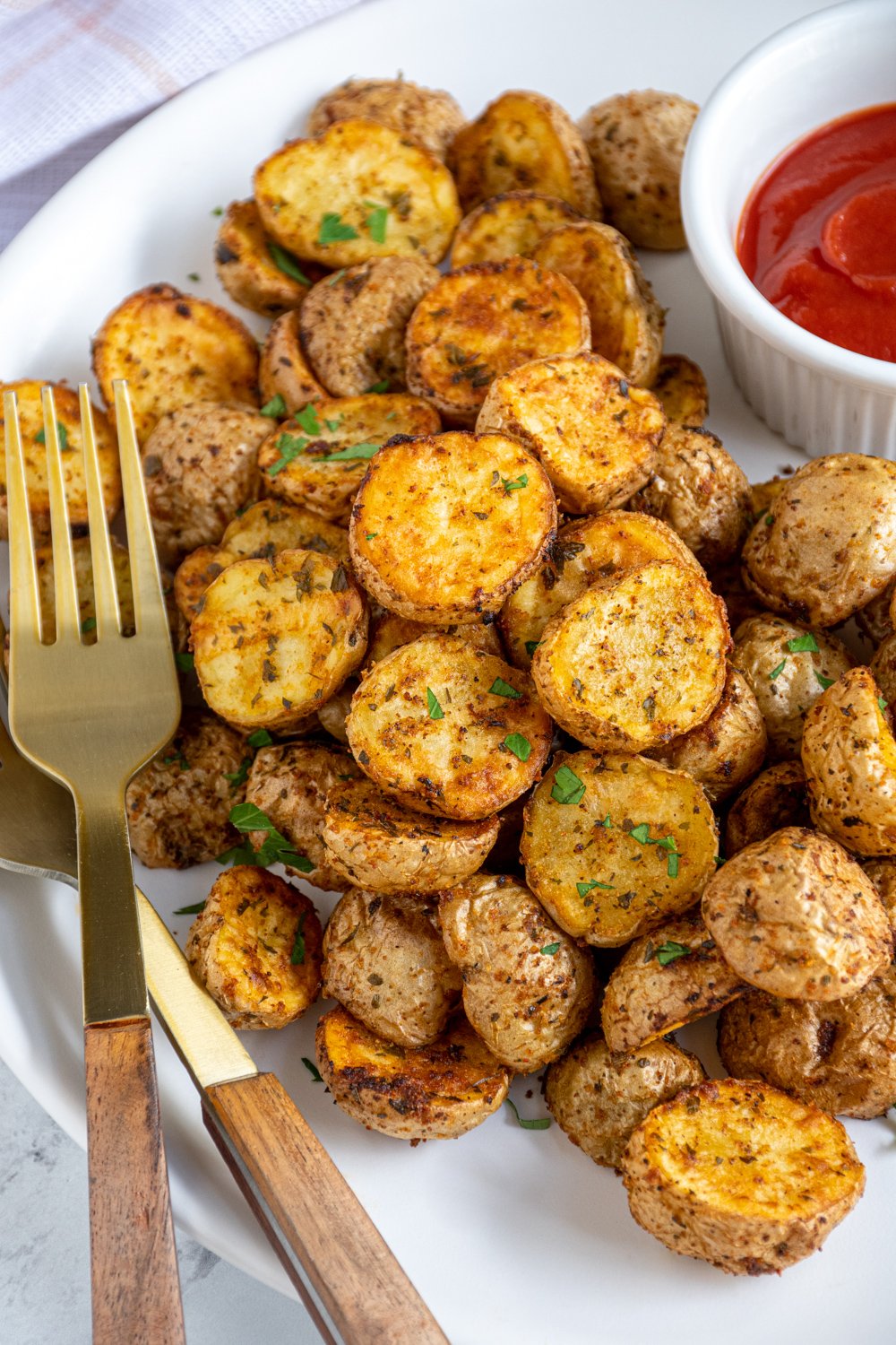 A plate filled with a pile of air fryer home fries with ketchup and a gold fork.