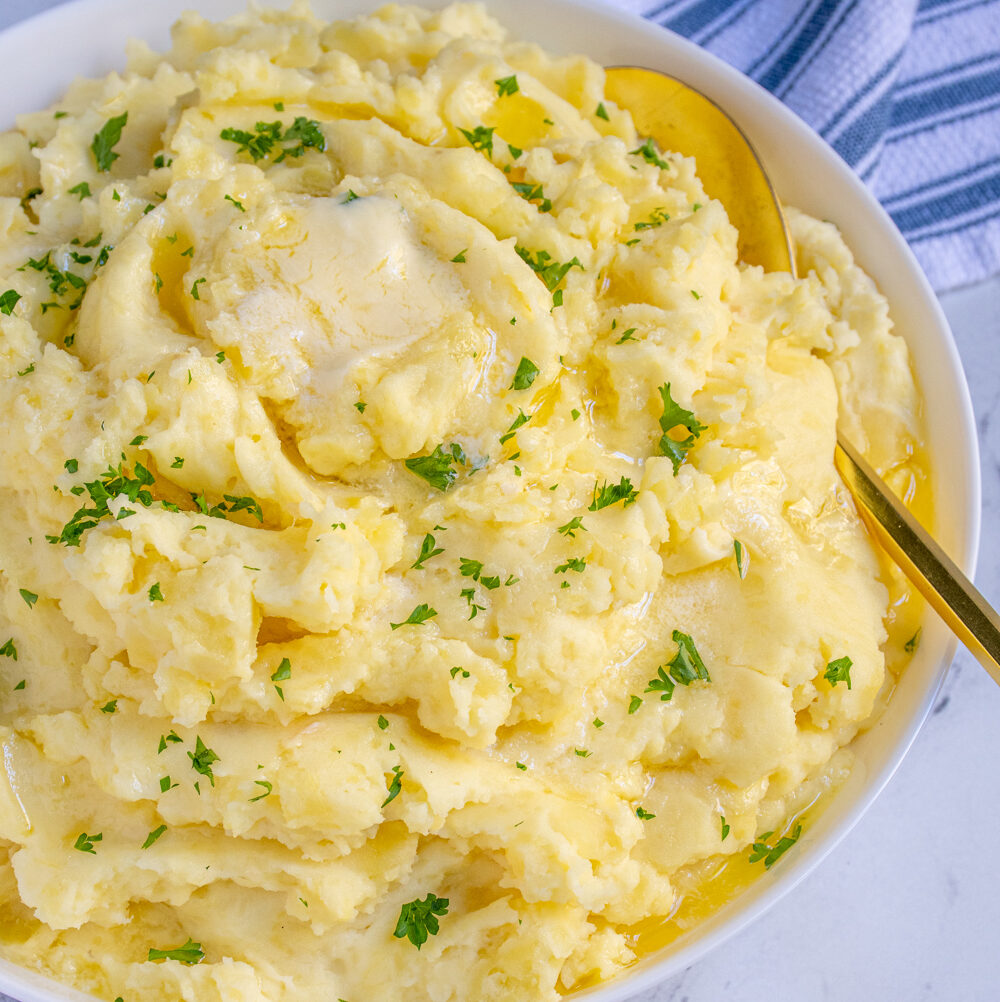 White bowl full of fluffy mashed potatoes dripping with melted butter and garnished with fresh parsley.