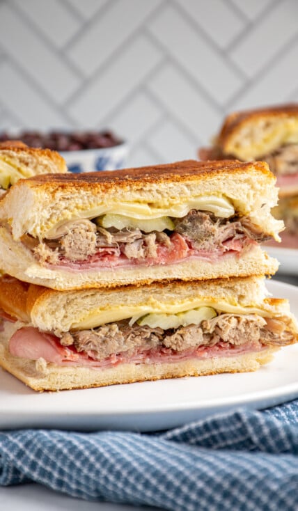 A Cuban sandwich sliced in half and stacked on top of one another showing the ingredients on the inside.