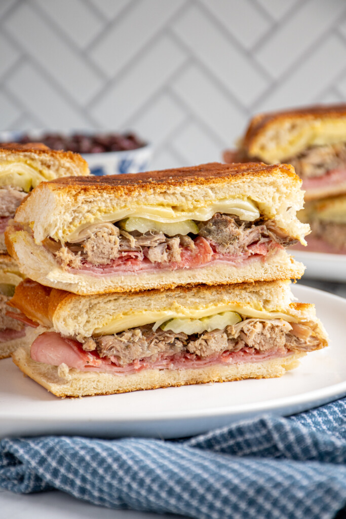 A Cuban sandwich sliced in half and stacked on top of one another showing the ingredients on the inside.