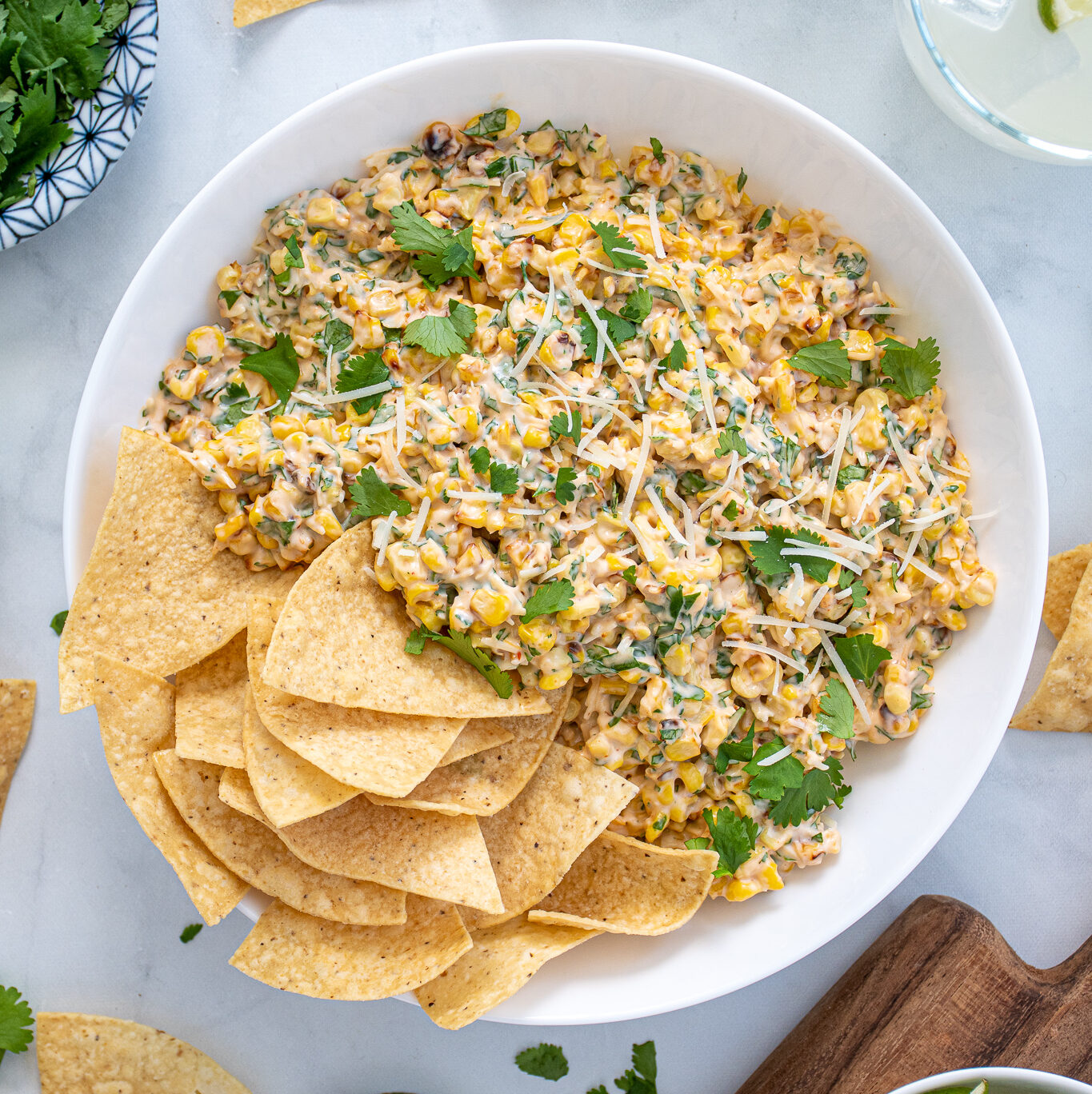 Large what bowl filled with Mexican Street Corn Dip and tortilla chips surrounded by more chips, cilantro, and limes.
