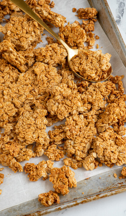Sheet pan filled with homemade peanut butter granola broken into big chunks by a gold spoon.
