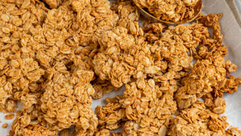 Sheet pan filled with homemade peanut butter granola broken into big chunks by a gold spoon.