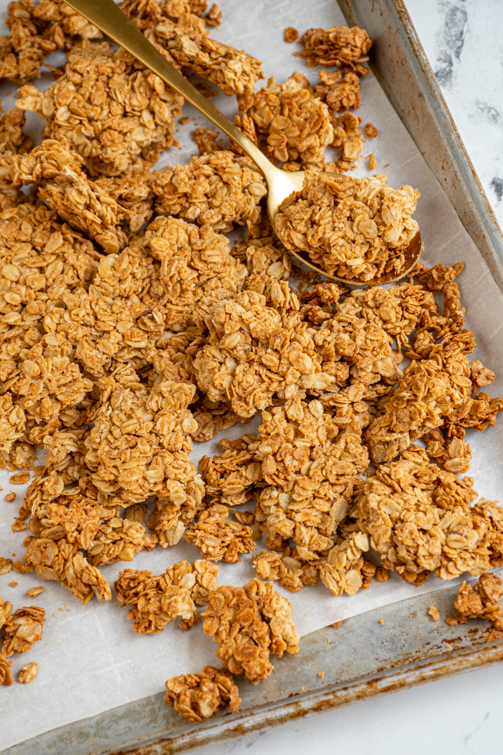 Sheet pan filled with homemade peanut butter granola broken into big chunks by a gold spoon.