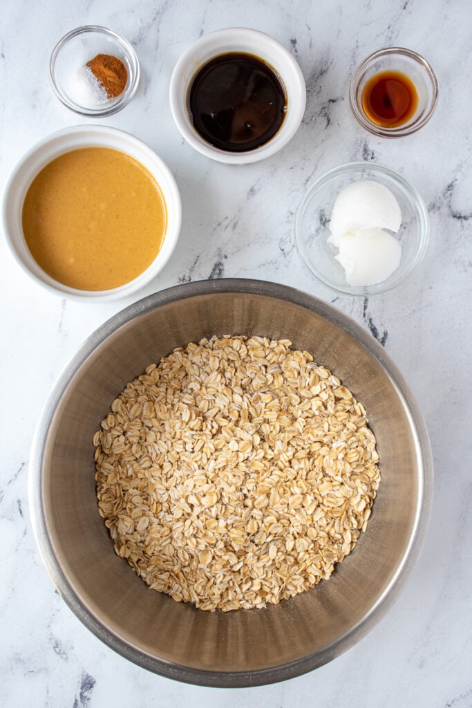 Ingredients for homemade peanut butter granola laid out on a tabletop in bowls.