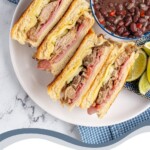 Pinterest Pin with text overlay 'Cuban sandwiches', image of a sandwich cut in half and stacked on top of each other showing off the insides.