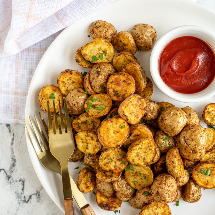 A white plate with gold forks and a pile of air fryer home fries next to a bowl of ketchup.