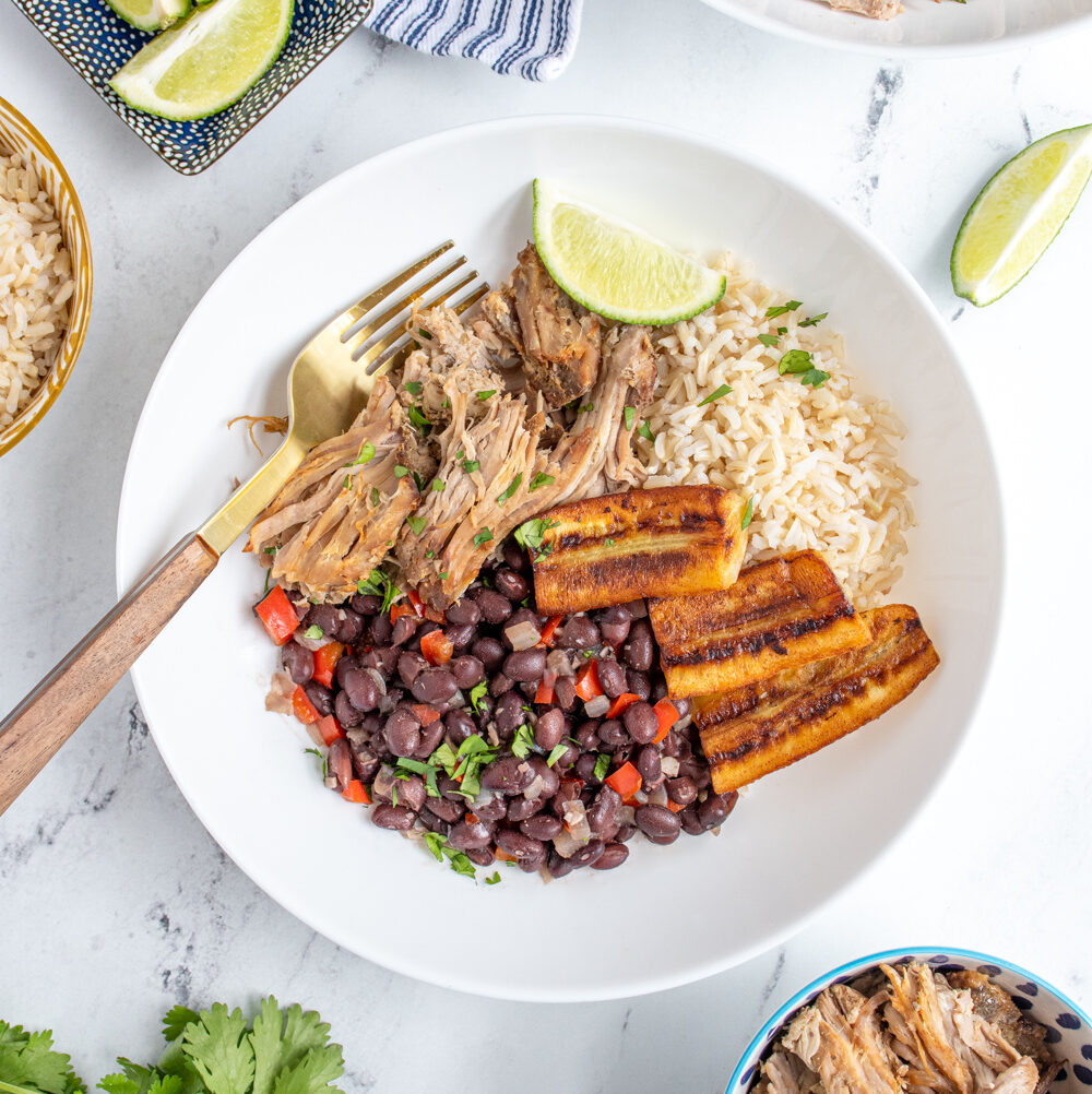 Overhead view of a cuban bowl filled with rice, mojo pork, black beans, and fried bananas.
