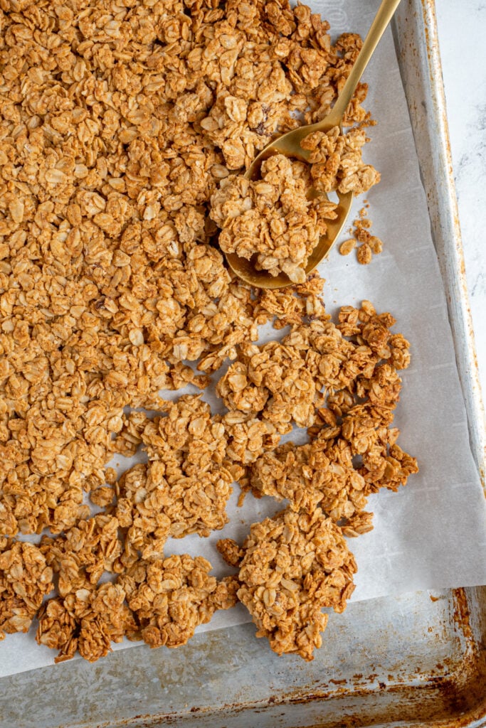 Close up of homemade peanut butter granola on a sheet pan, some of it broken into clusters.