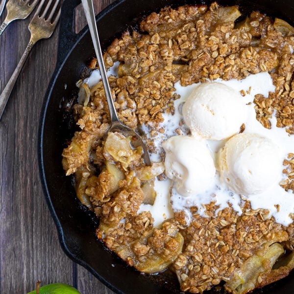overhead shot of a cast iron on a table filled with apple crisp topped with ice cream and part of it scooped up with a spoon