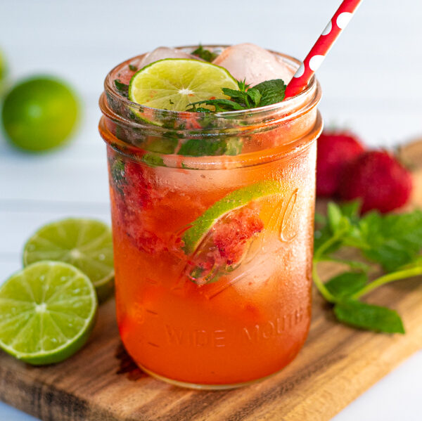 drinking glass jar filled with a bright pink Strawberry Mojito Mocktail made with lime seltzer and garnished with lime slices and fresh mint leaves
