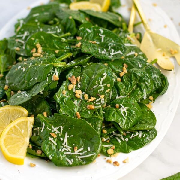 a white platter full of simple spinach salad with cheese and walnuts