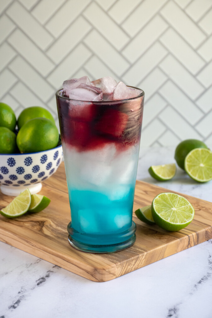 A highball glass on a cutting board filled with red, white, and blue layers of a margarita.