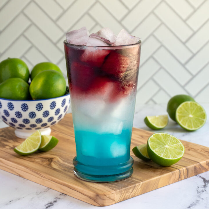 A highball glass filled with ice and layers of a red, white, and blue margarita.
