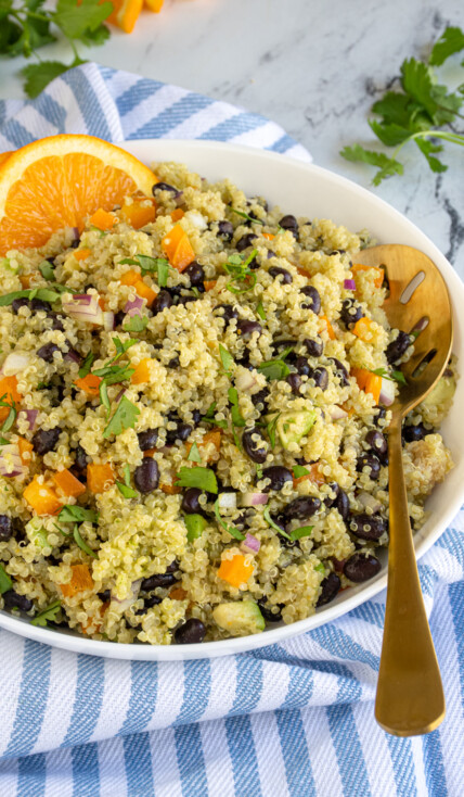 A white serving bowl filled with black bean quinoa salad with orange cilantro dressing and garnished with orange slices and cilantro.