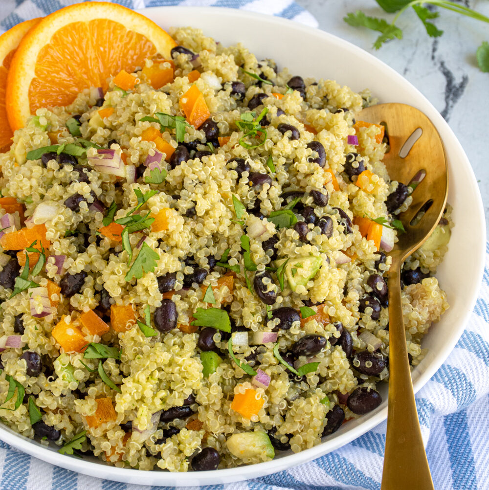 A white serving bowl filled with black bean quinoa salad with orange cilantro dressing and garnished with orange slices and cilantro.